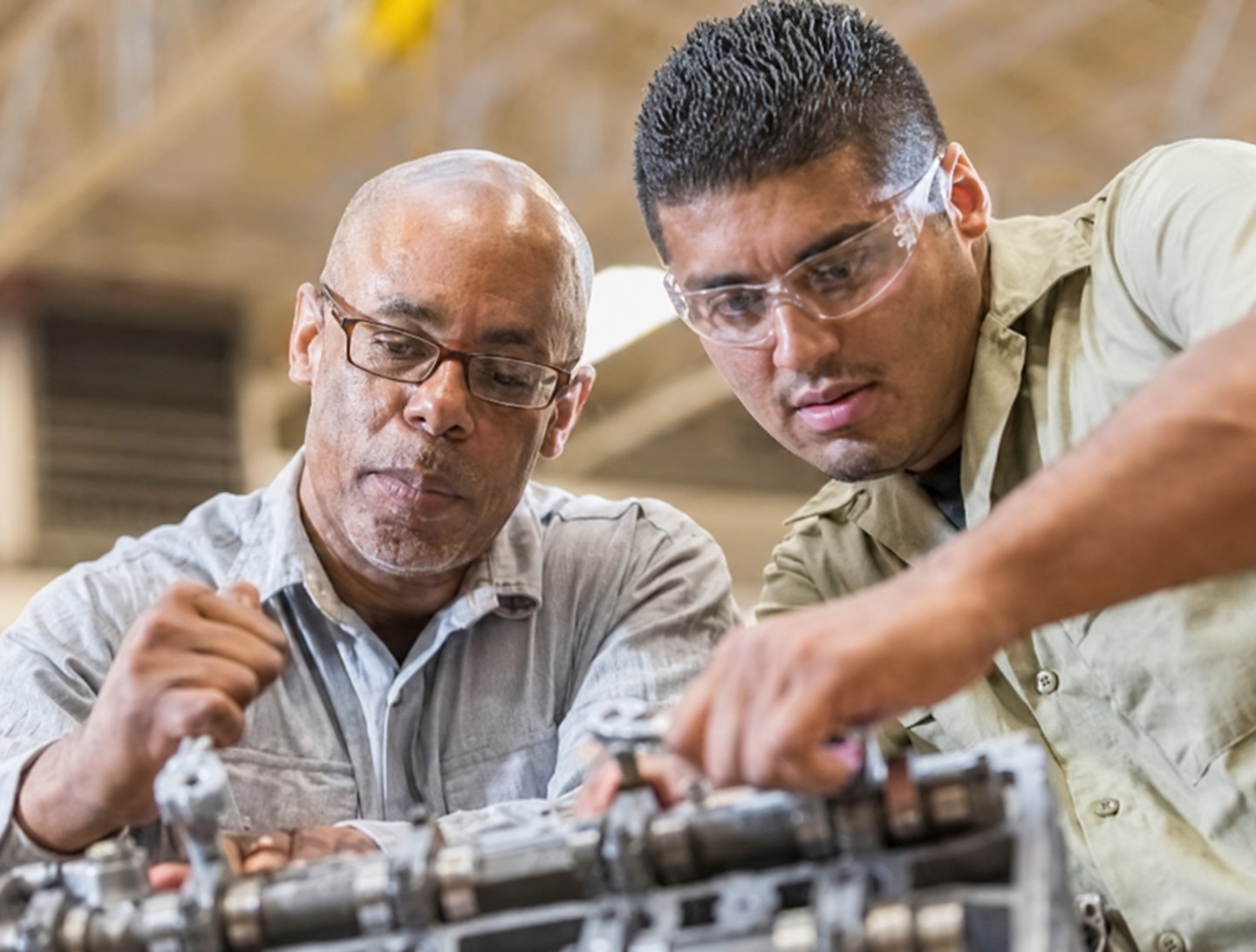 Two Hispanic tradesmen working together on an engine in a workshop — the businesses Alante serves